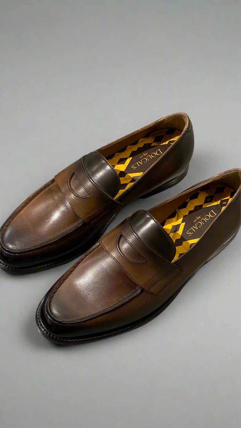 Brown leather loafers with yellow accents on a reflective surface