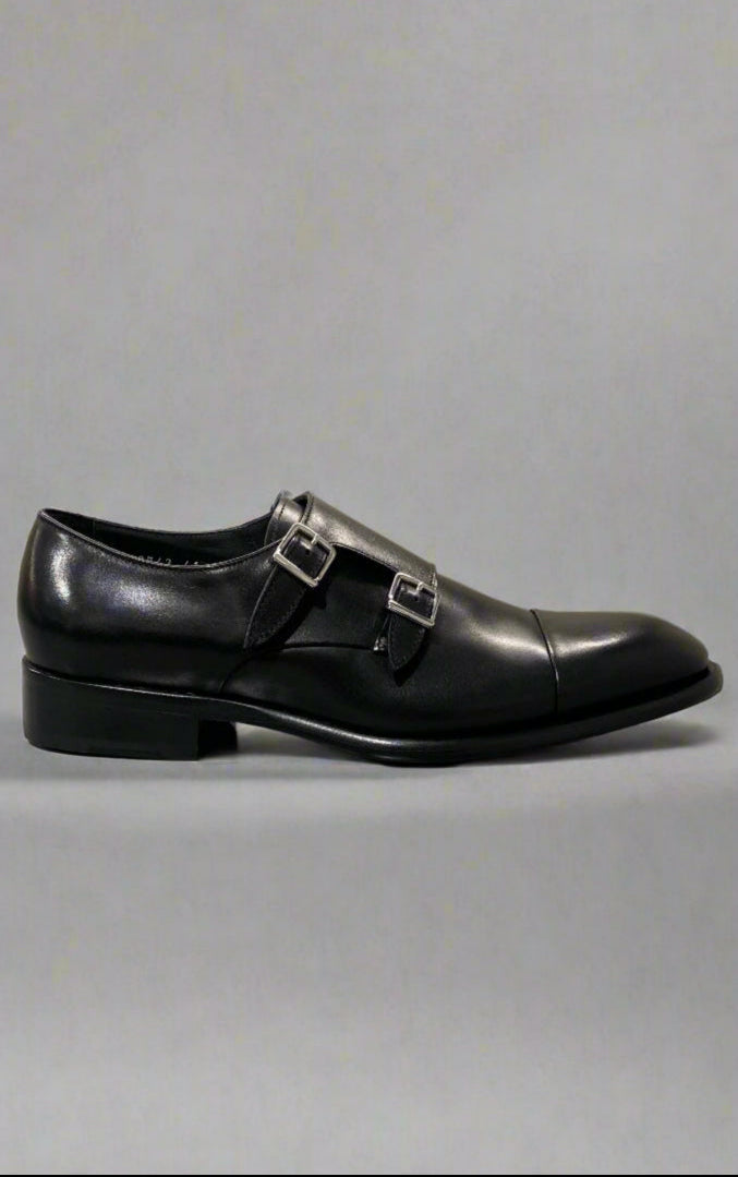 Black leather dress shoe with a buckle on a reflective surface