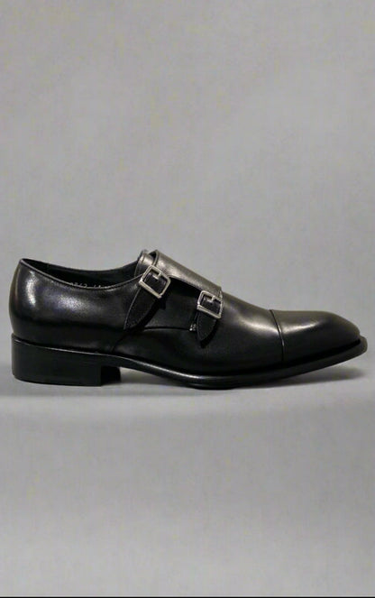 Black leather dress shoe with a buckle on a reflective surface