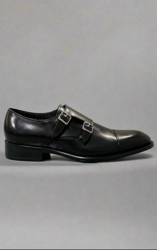 Black leather dress shoe with a buckle on a reflective surface